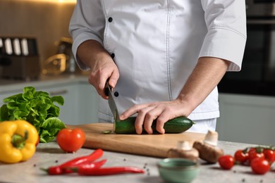 Photo of Professional chef cutting zucchini at table in kitchen, closeup