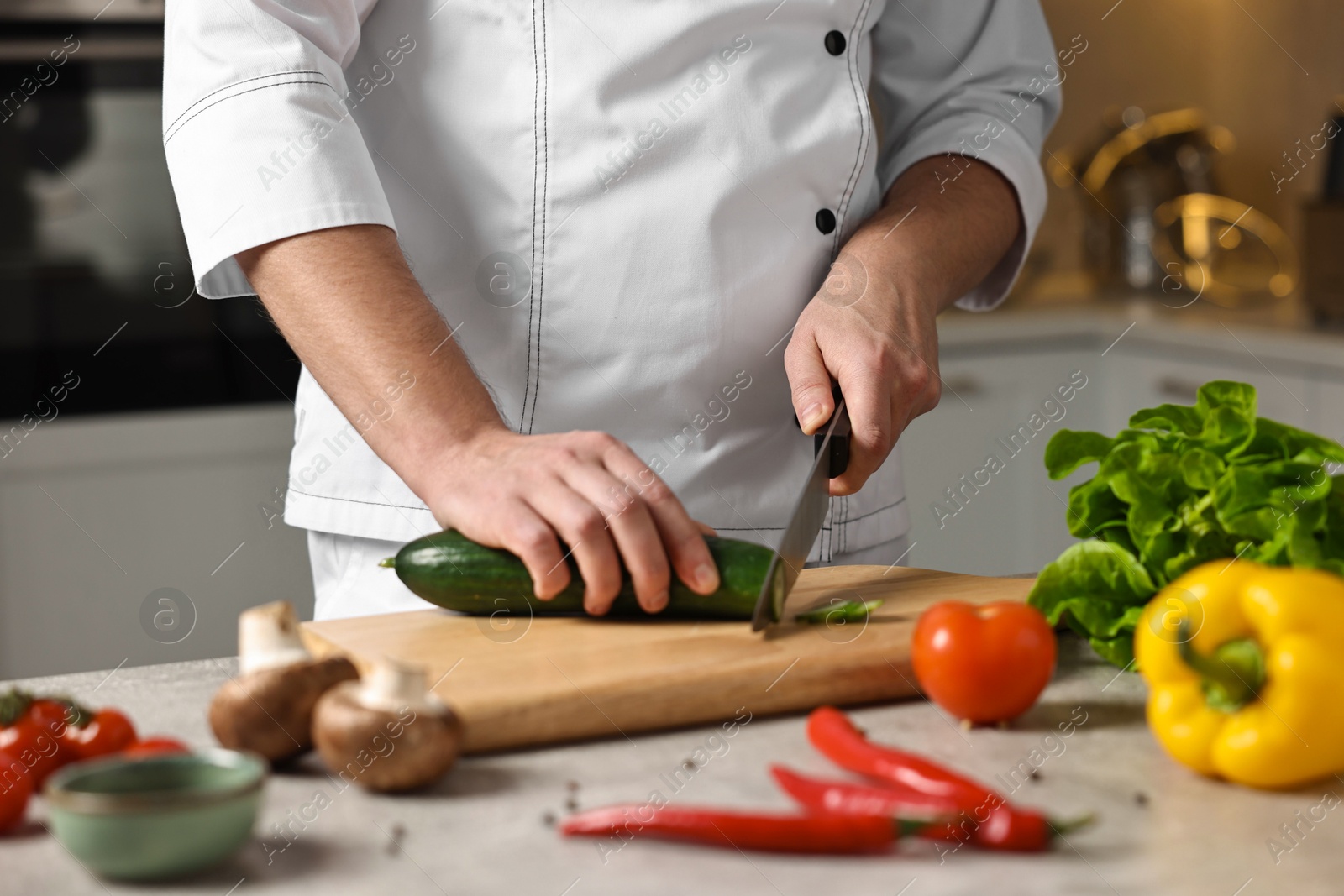 Photo of Professional chef cutting zucchini at table in kitchen, closeup