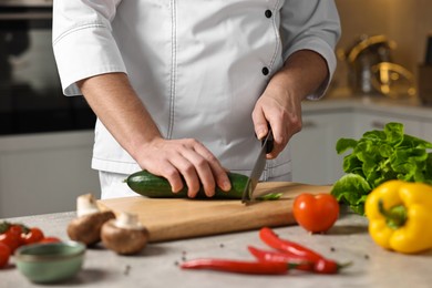 Photo of Professional chef cutting zucchini at table in kitchen, closeup