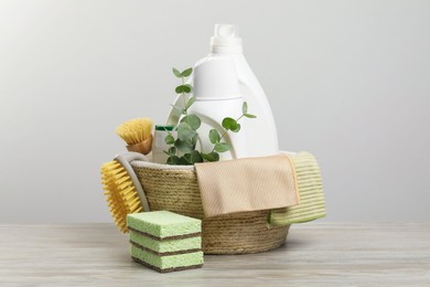 Photo of Eco-friendly cleaning products, supplies and eucalyptus branches in wicker basket on wooden table