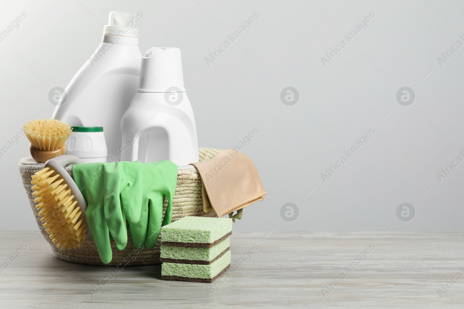 Photo of Eco-friendly cleaning products and supplies in wicker basket on wooden table, space for text