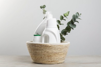 Photo of Eco-friendly cleaning products and eucalyptus branches in wicker basket on wooden table