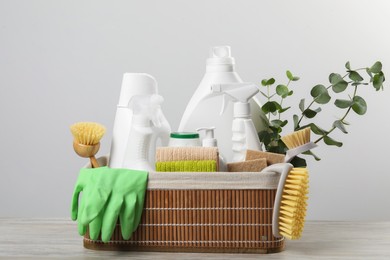 Photo of Eco-friendly cleaning products, supplies and eucalyptus branches in wicker basket on wooden table