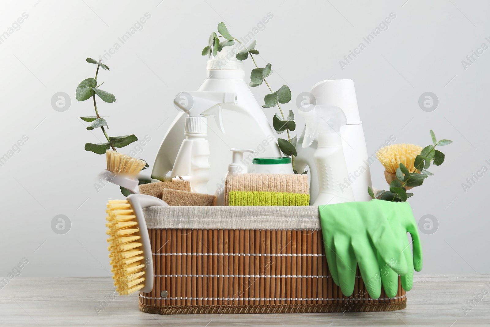 Photo of Eco-friendly cleaning products, supplies and eucalyptus branches in wicker basket on wooden table