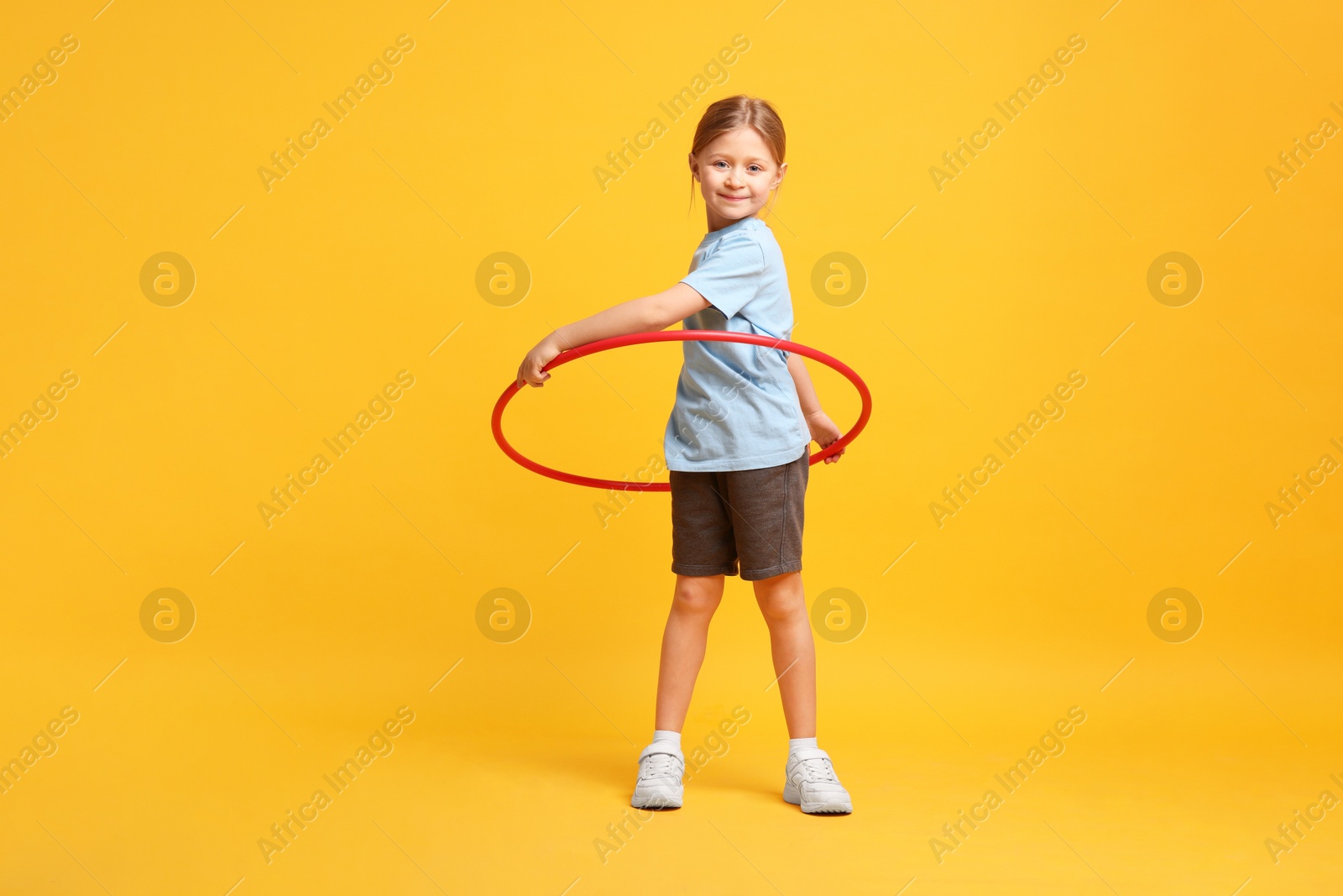 Photo of Cute little girl exercising with hula hoop on orange background