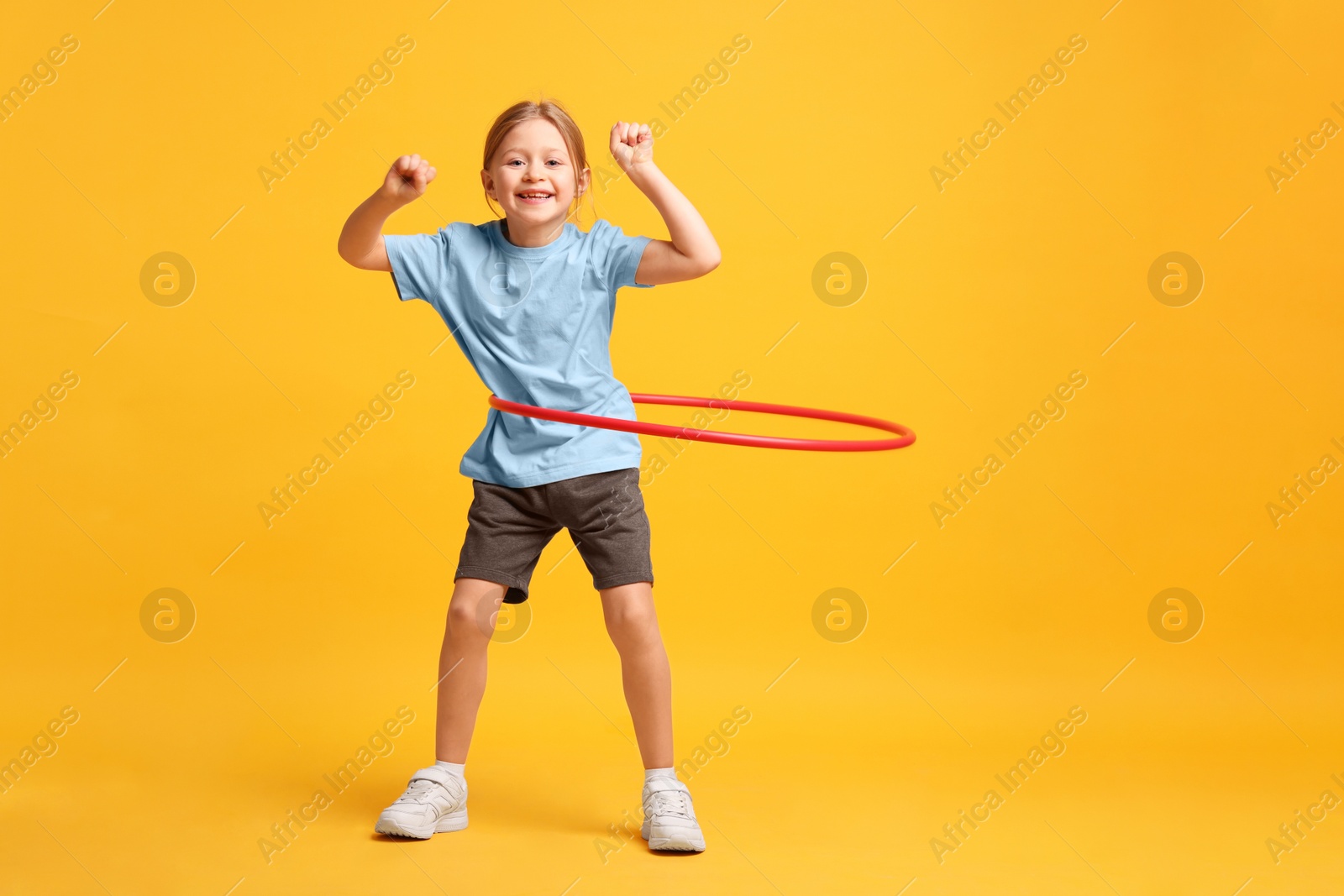 Photo of Cute little girl exercising with hula hoop on orange background