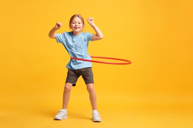 Photo of Cute little girl exercising with hula hoop on orange background