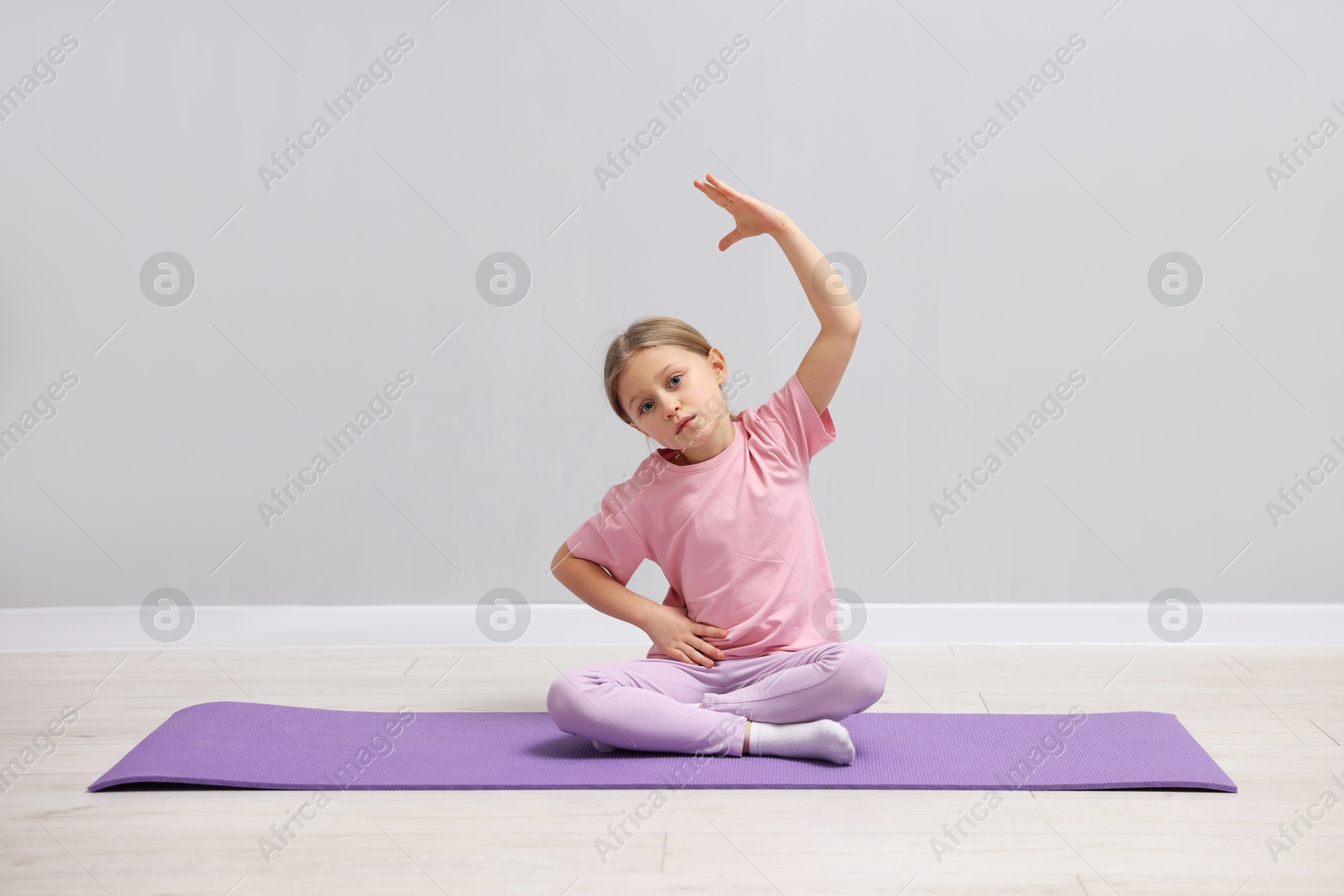 Photo of Cute little girl exercising on fitness mat near grey wall indoors