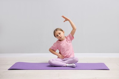 Photo of Cute little girl exercising on fitness mat near grey wall indoors