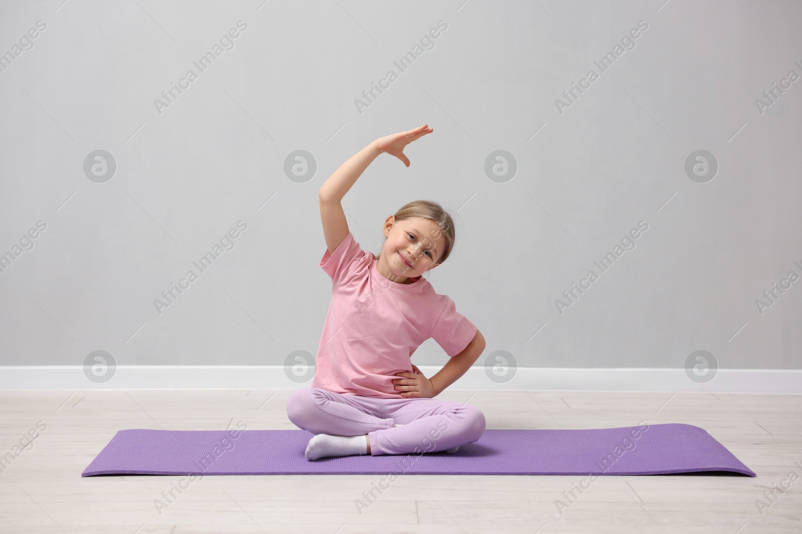 Photo of Cute little girl exercising on fitness mat near grey wall indoors