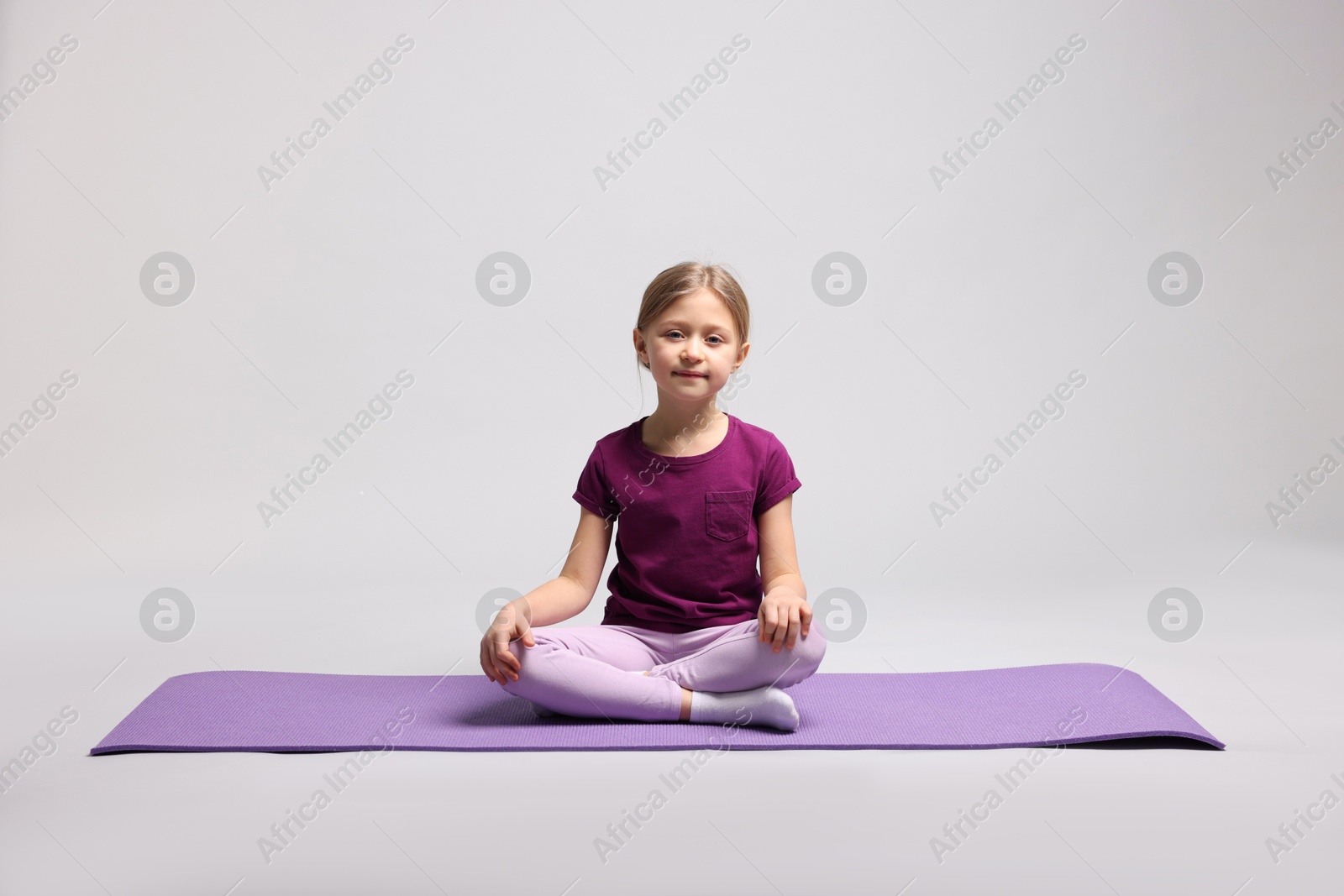 Photo of Cute little girl exercising on fitness mat against light grey background