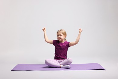 Photo of Cute little girl exercising on fitness mat against light grey background