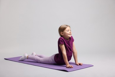 Photo of Cute little girl exercising on fitness mat against light grey background