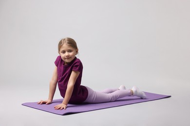 Photo of Cute little girl exercising on fitness mat against light grey background