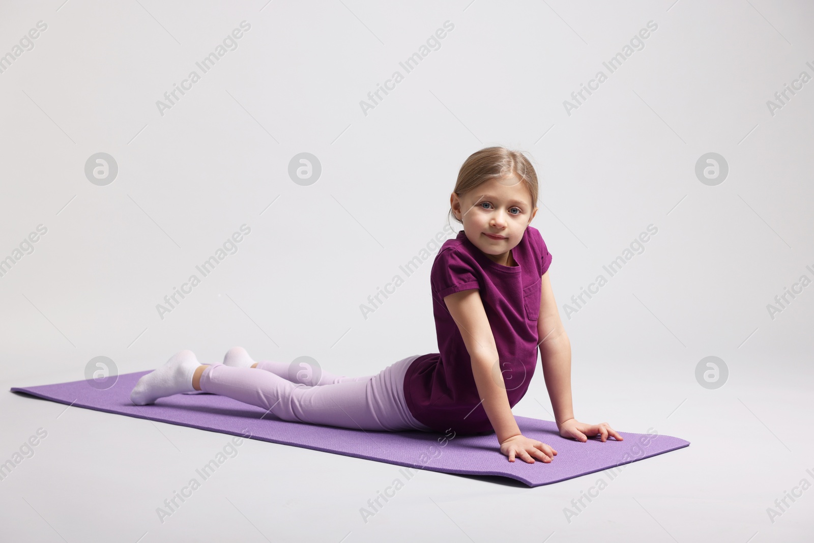 Photo of Cute little girl exercising on fitness mat against light grey background