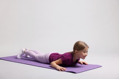 Photo of Cute little girl exercising on fitness mat against light grey background