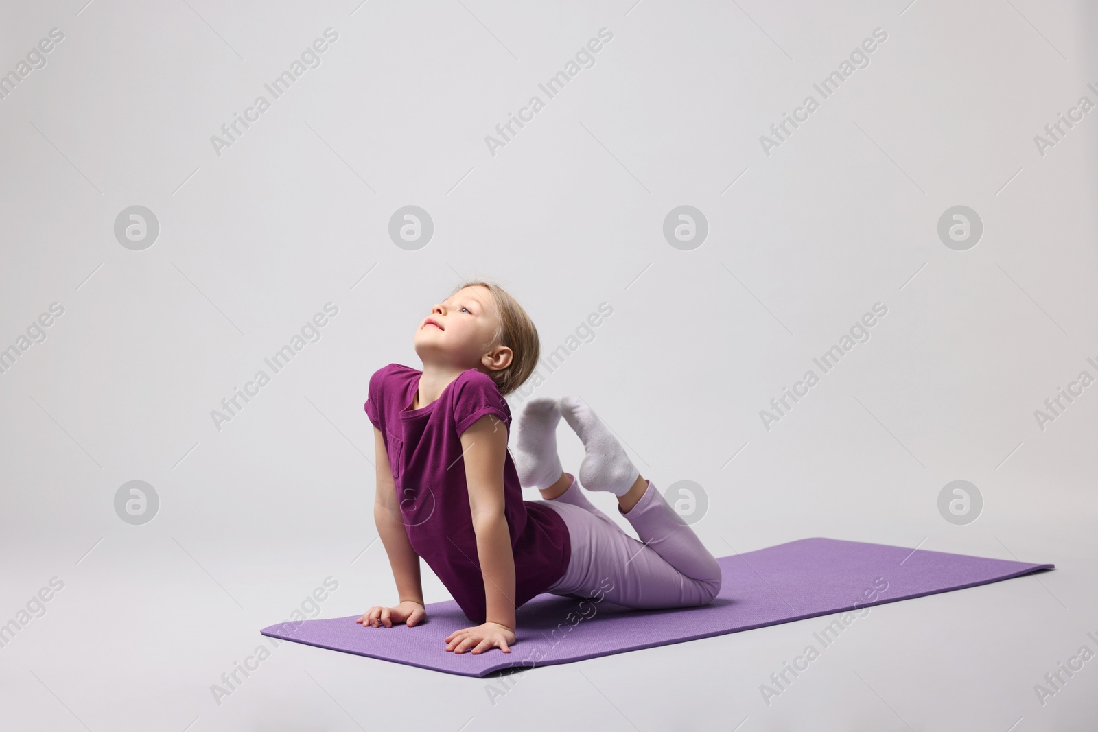 Photo of Cute little girl exercising on fitness mat against light grey background