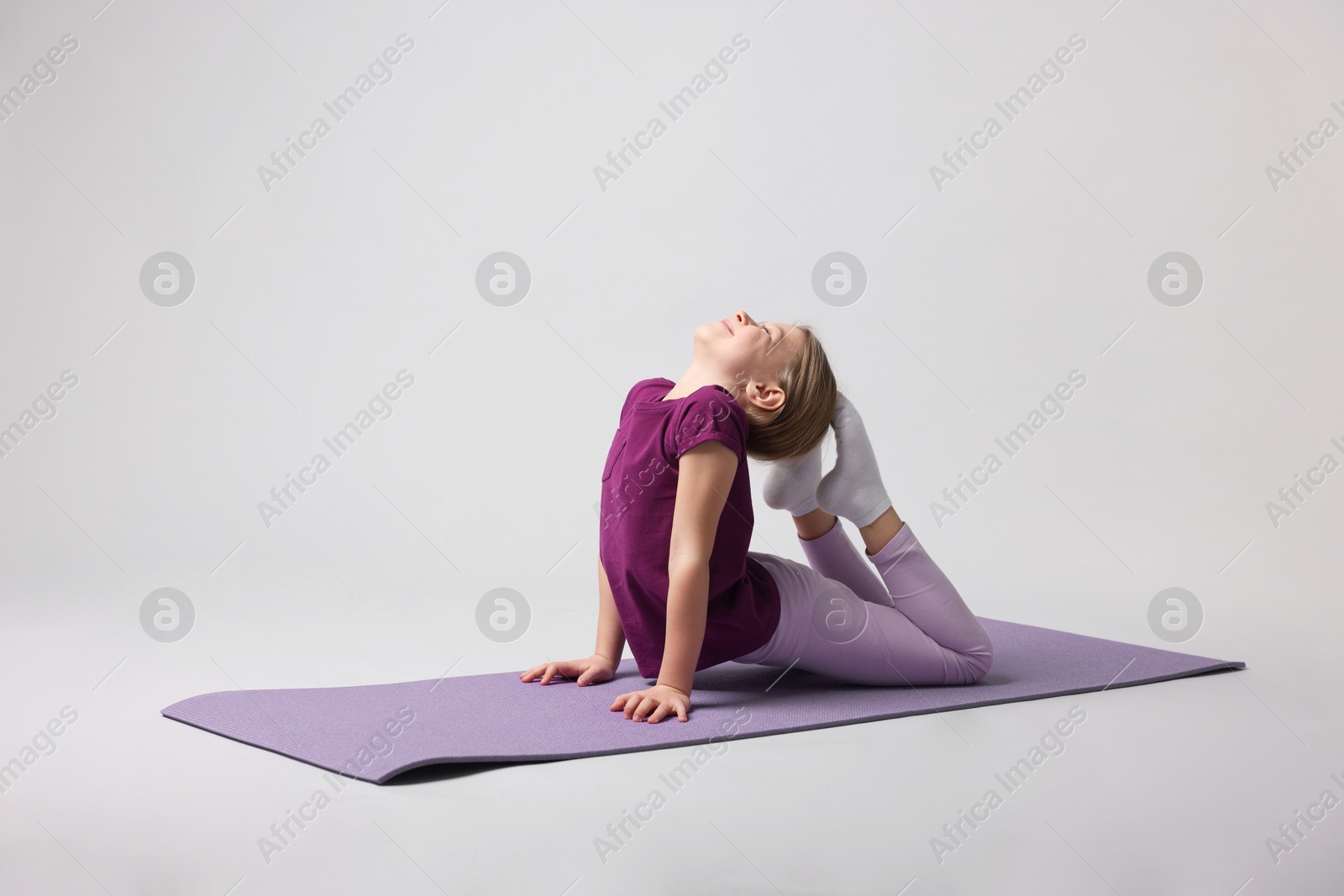 Photo of Cute little girl exercising on fitness mat against light grey background, space for text