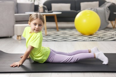 Photo of Cute little girl exercising on fitness mat indoors