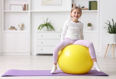 Photo of Cute little girl with fitness ball indoors, space for text