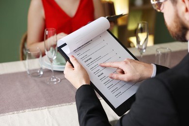 Couple choosing dishes from menu at table in restaurant, closeup