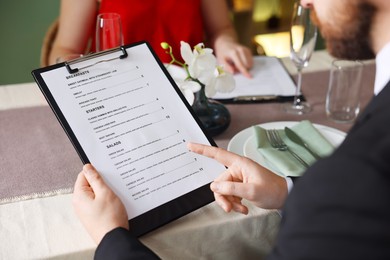 Photo of Couple choosing dishes from menu at table in restaurant, closeup