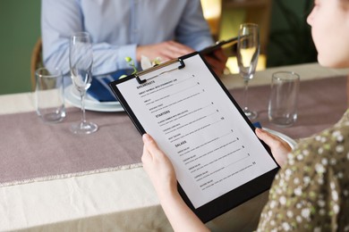 Photo of Couple choosing dishes from menu at table in restaurant, closeup