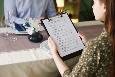 Photo of Couple choosing dishes from menu at table in restaurant, closeup