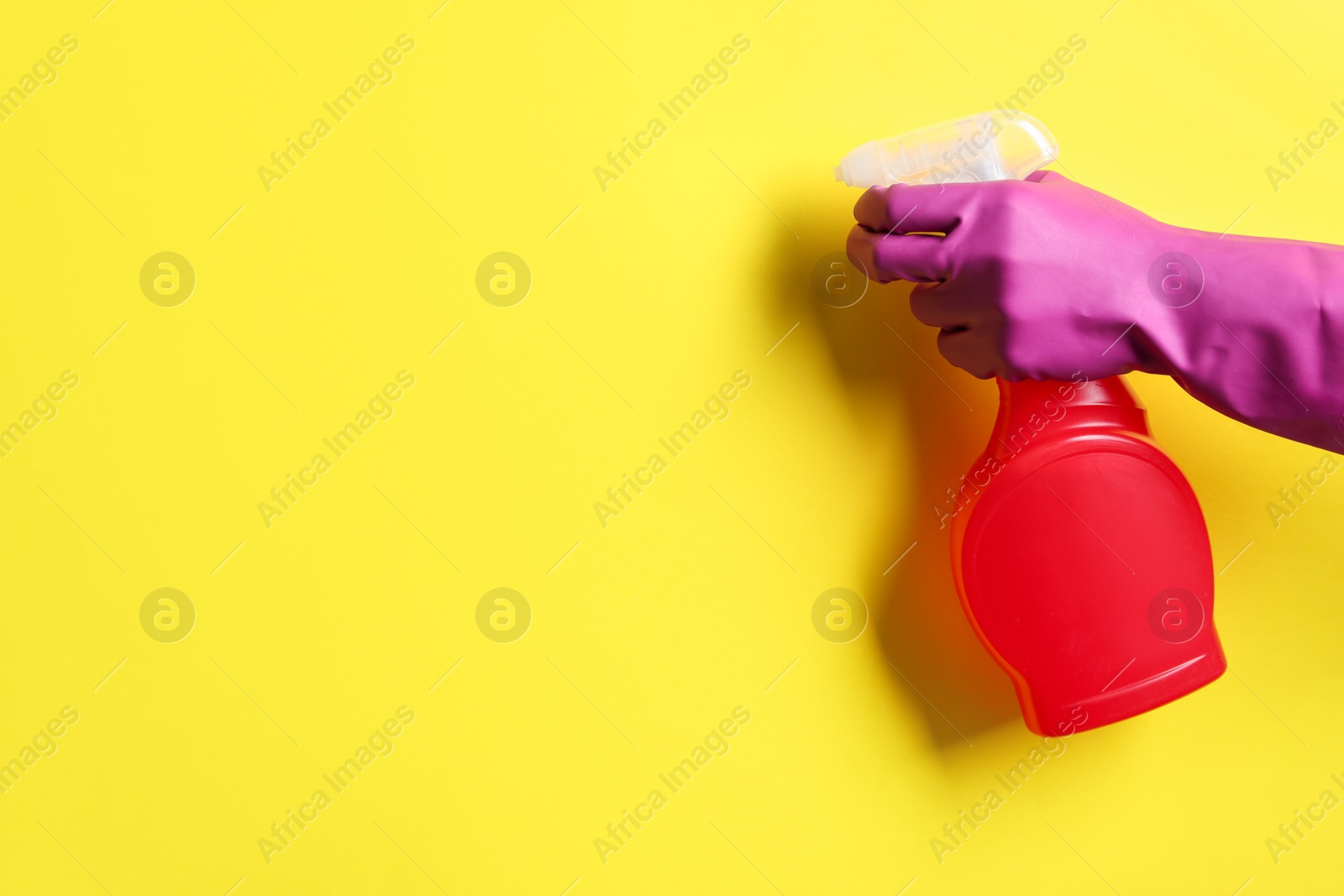 Photo of Woman with spray bottle of cleaning product on yellow background, closeup. Space for text