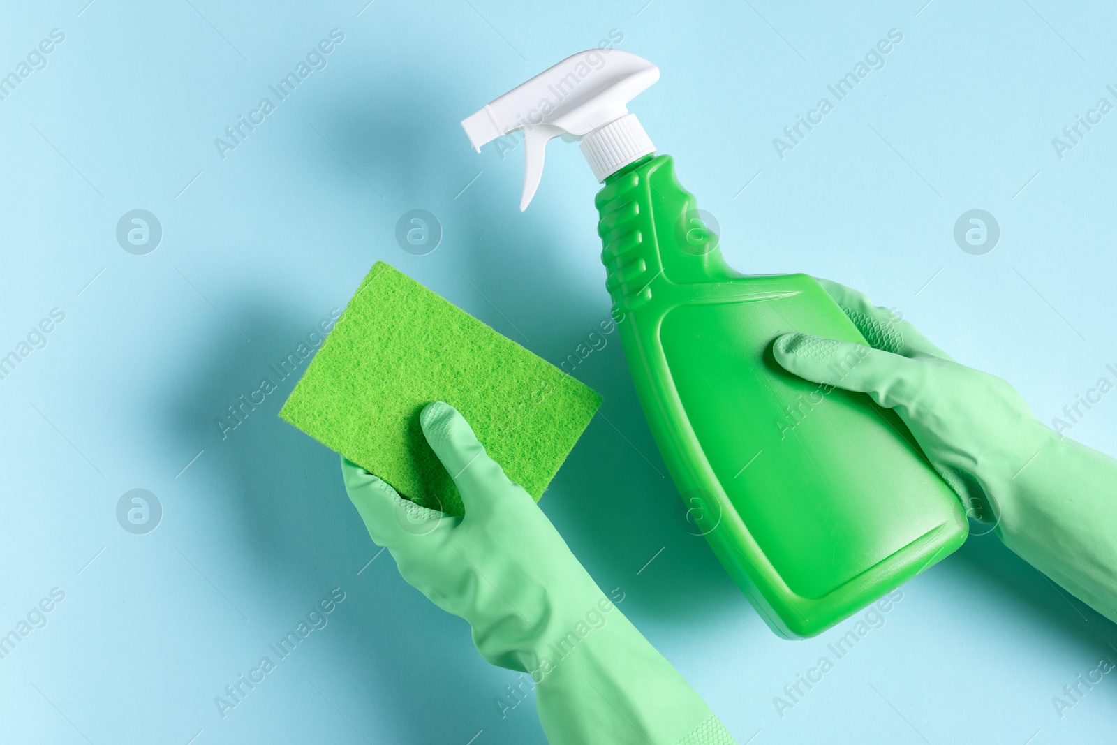 Photo of Woman with bottle of cleaning product and sponge on light blue background, top view