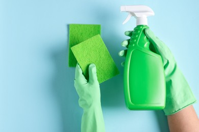 Photo of Woman with bottle of cleaning product and sponges on light blue background, top view. Space for text