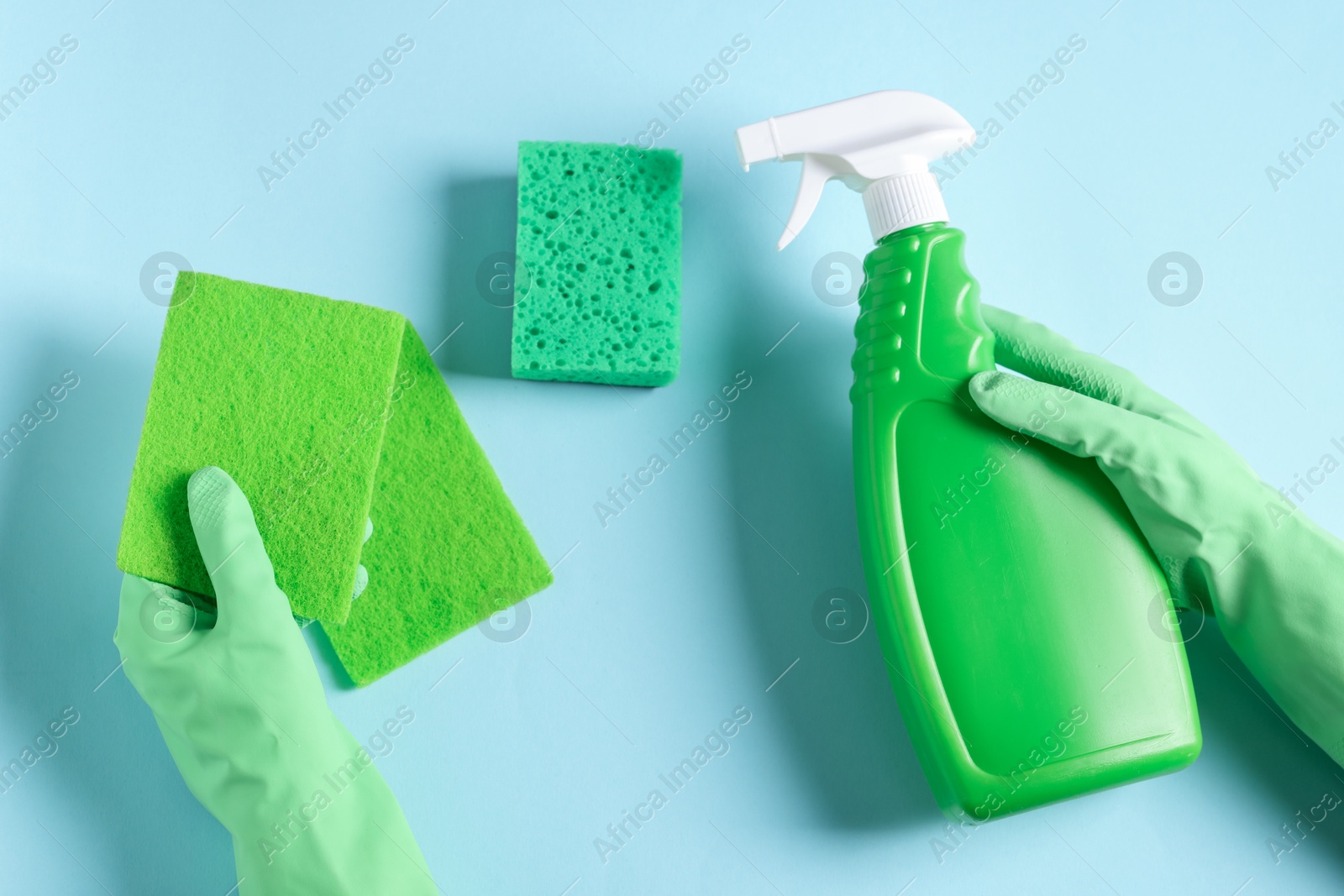 Photo of Woman with bottle of cleaning product and sponges on light blue background, top view