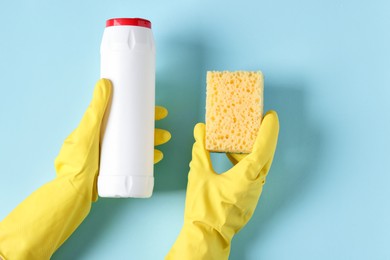 Photo of Woman with bottle of cleaning product and sponge on light blue background, top view