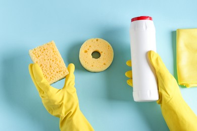 Photo of Woman with bottle of cleaning product and supplies on light blue background, top view