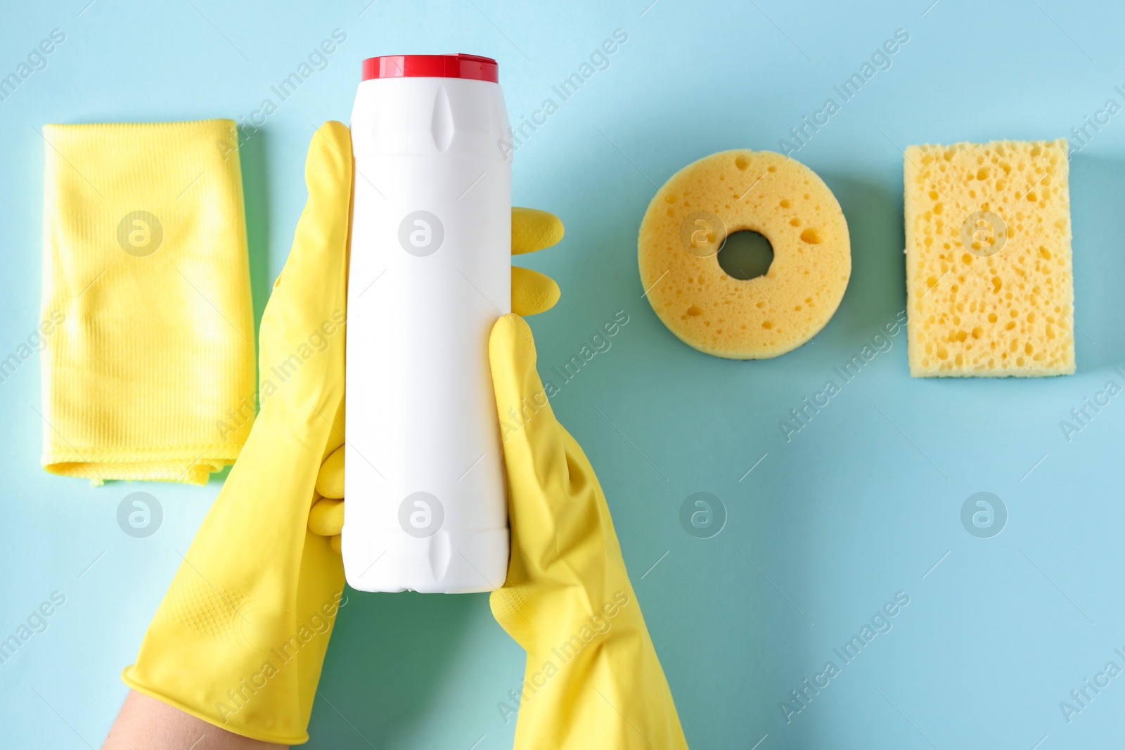 Photo of Woman with bottle of cleaning product and supplies on light blue background, top view