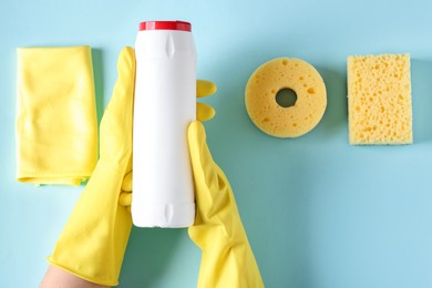 Photo of Woman with bottle of cleaning product and supplies on light blue background, top view