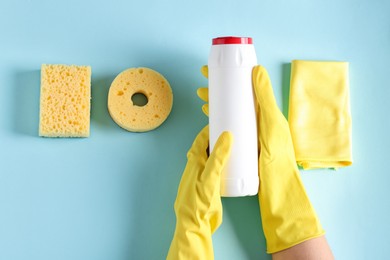 Photo of Woman with bottle of cleaning product and supplies on light blue background, top view