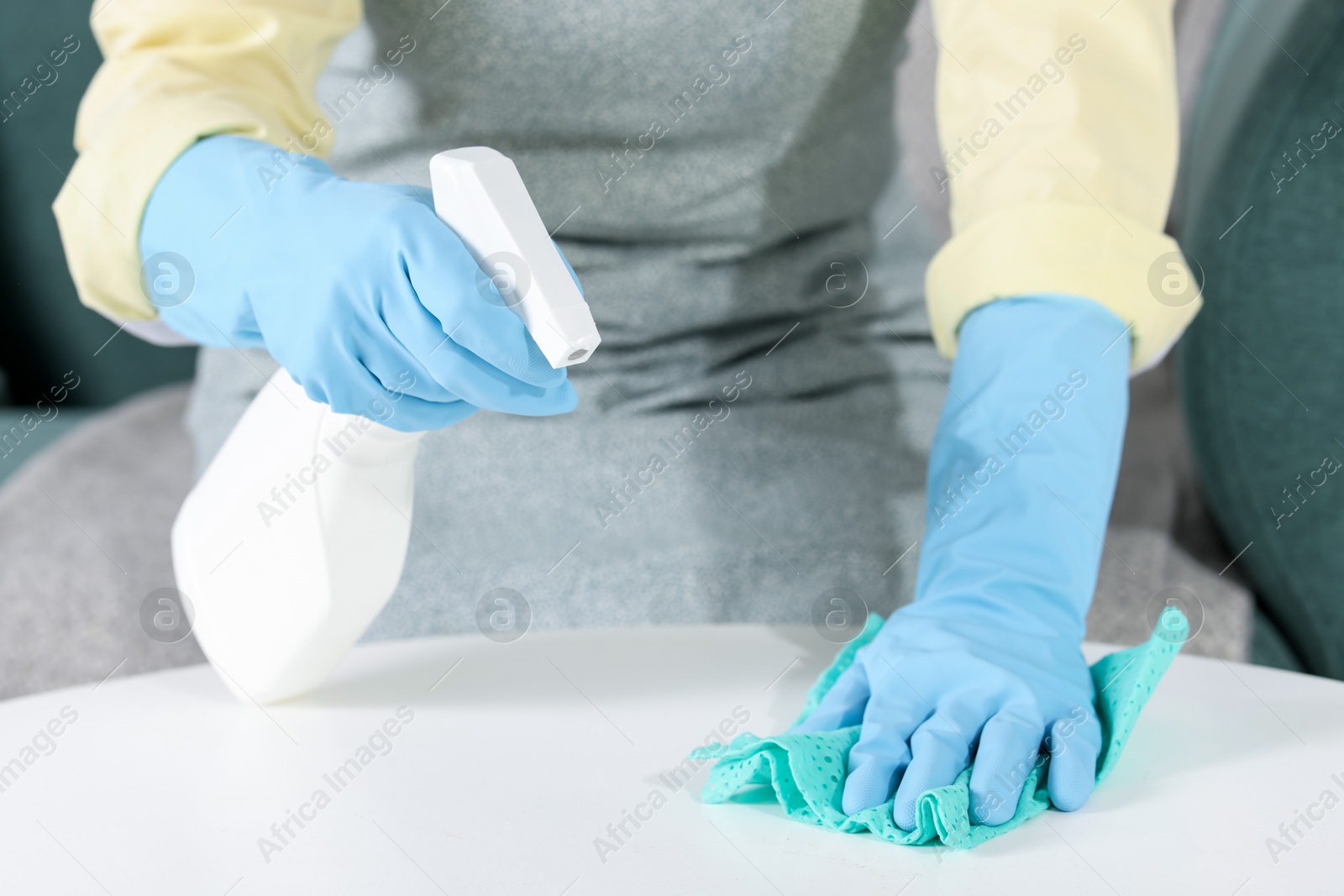 Photo of Woman using cleaning product while wiping table with rag indoors, closeup