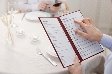 Photo of Man with menu at table in restaurant, closeup