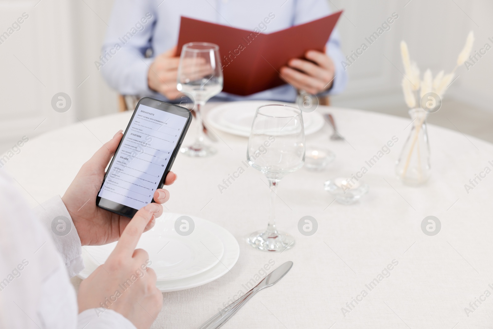 Photo of Woman viewing menu on smartphone at table in restaurant, closeup