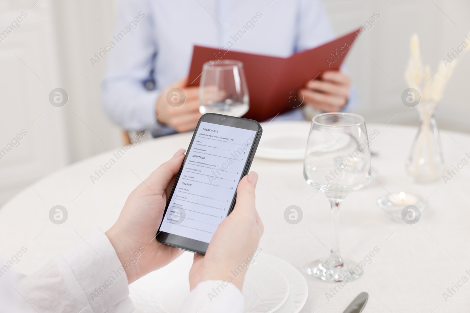 Photo of Woman viewing menu on smartphone at table in restaurant, closeup