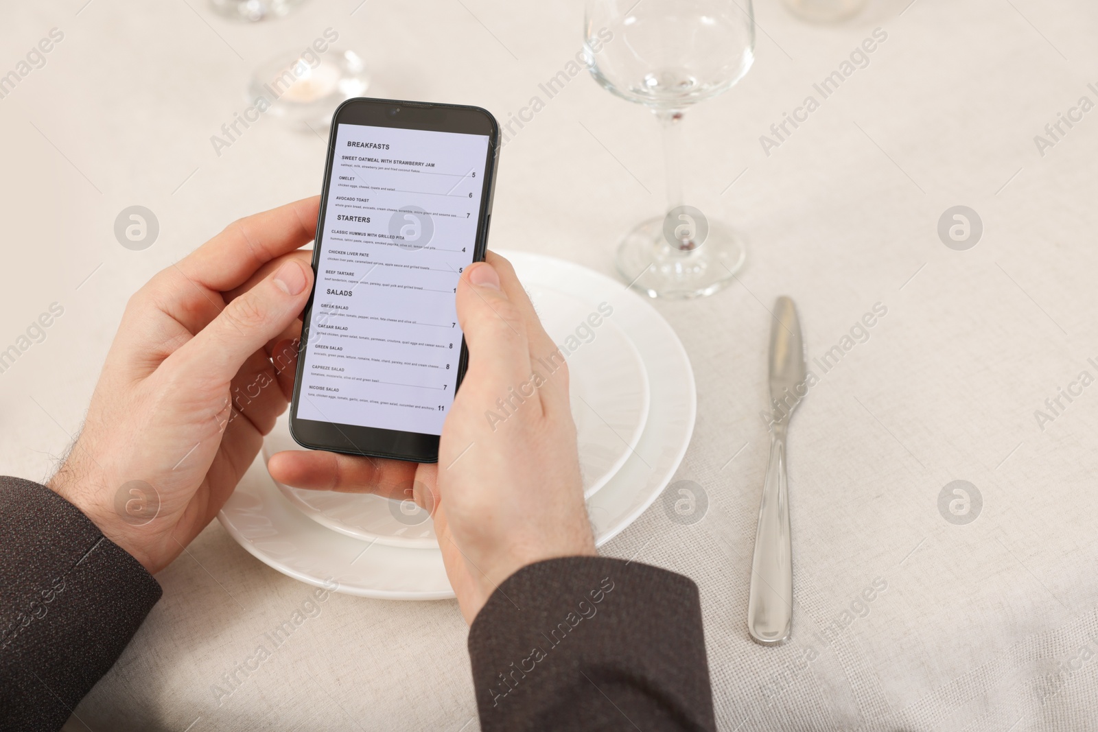 Photo of Man viewing menu on smartphone at table in restaurant, closeup