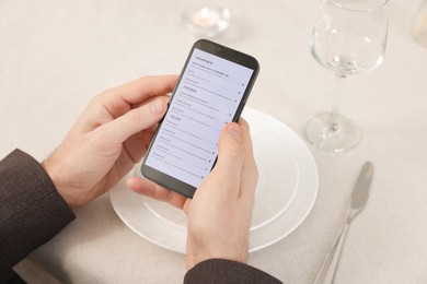 Photo of Man viewing menu on smartphone at table in restaurant, closeup