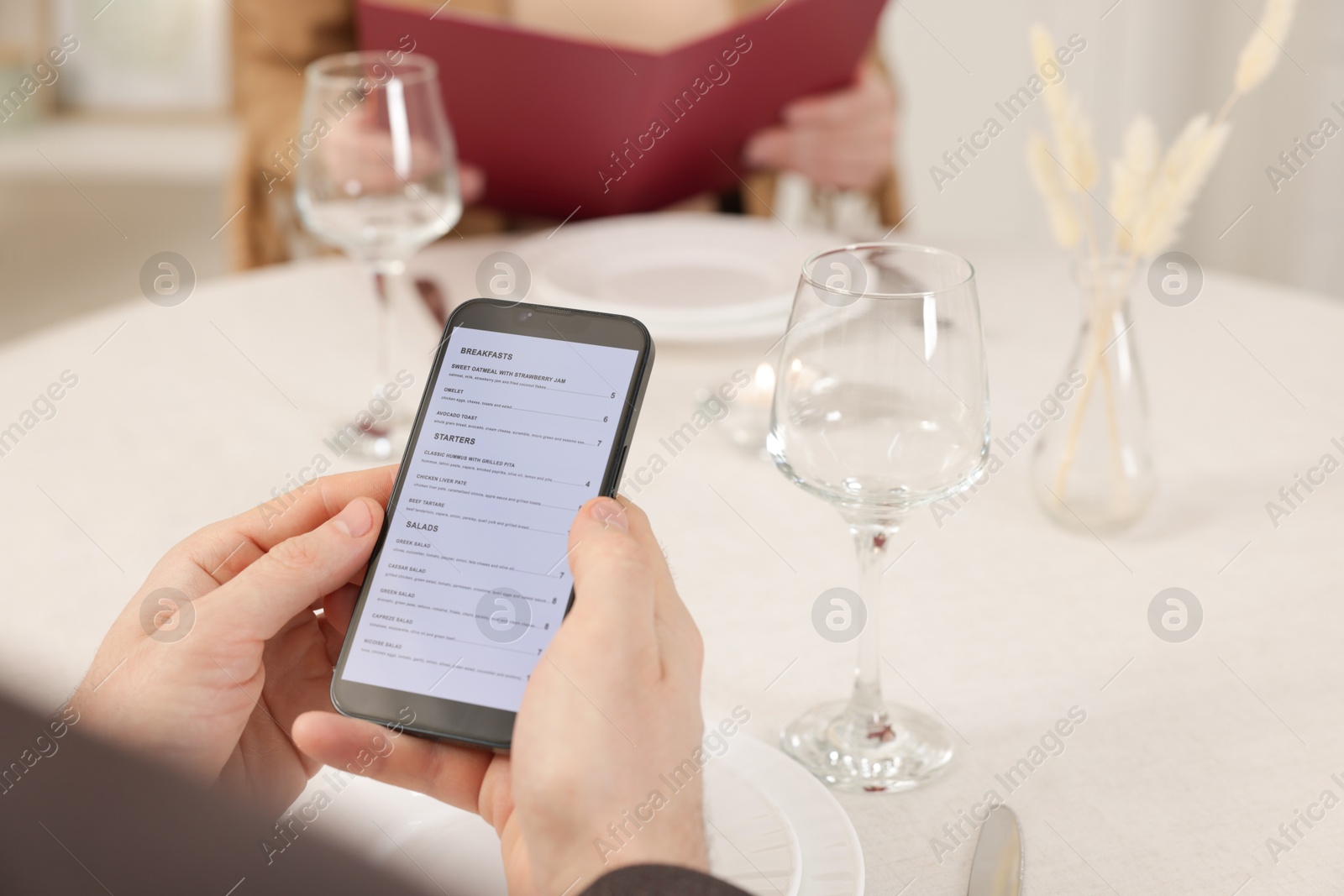 Photo of Man viewing menu on smartphone at table in restaurant, closeup