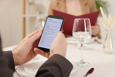 Photo of Man viewing menu on smartphone at table in restaurant, closeup