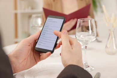 Photo of Man viewing menu on smartphone at table in restaurant, closeup