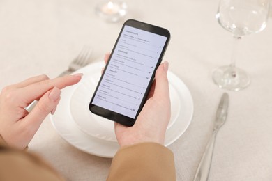 Photo of Woman viewing menu on smartphone at table in restaurant, closeup