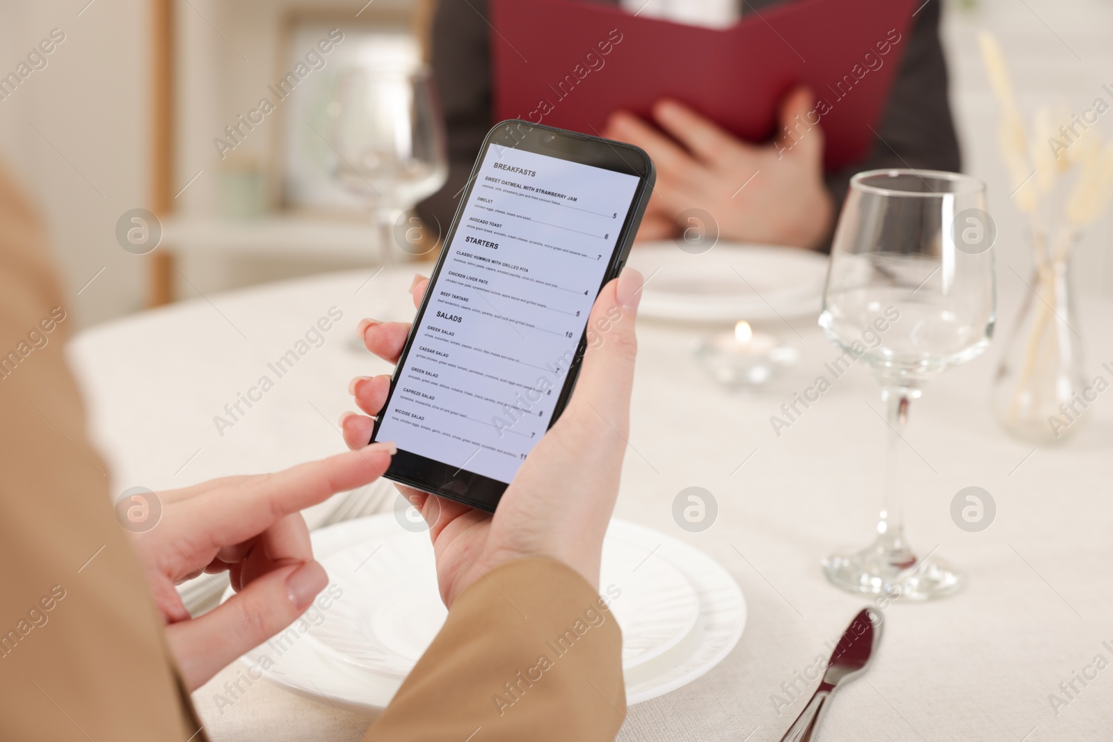 Photo of Woman viewing menu on smartphone at table in restaurant, closeup