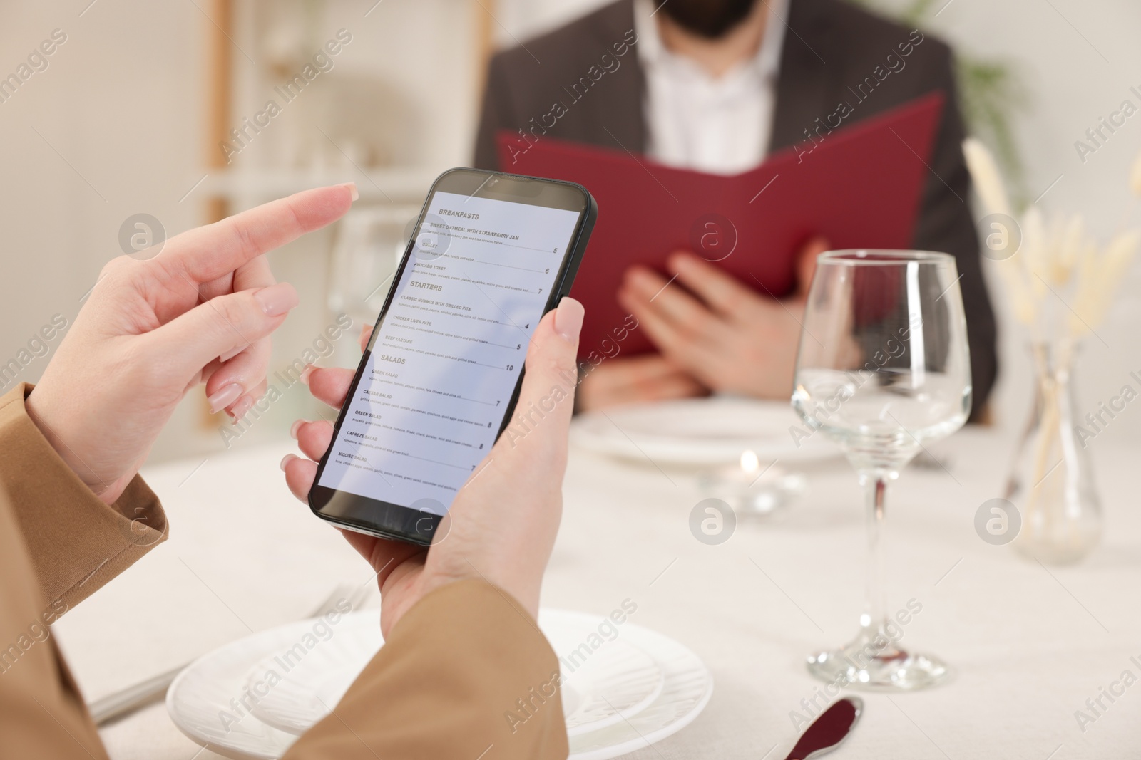 Photo of Woman viewing menu on smartphone at table in restaurant, closeup