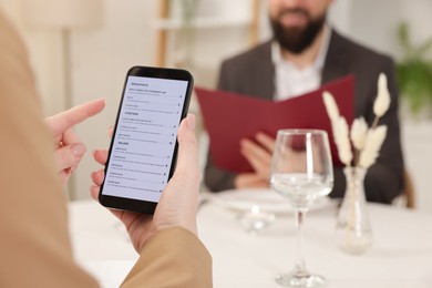 Photo of Woman viewing menu on smartphone at table in restaurant, closeup